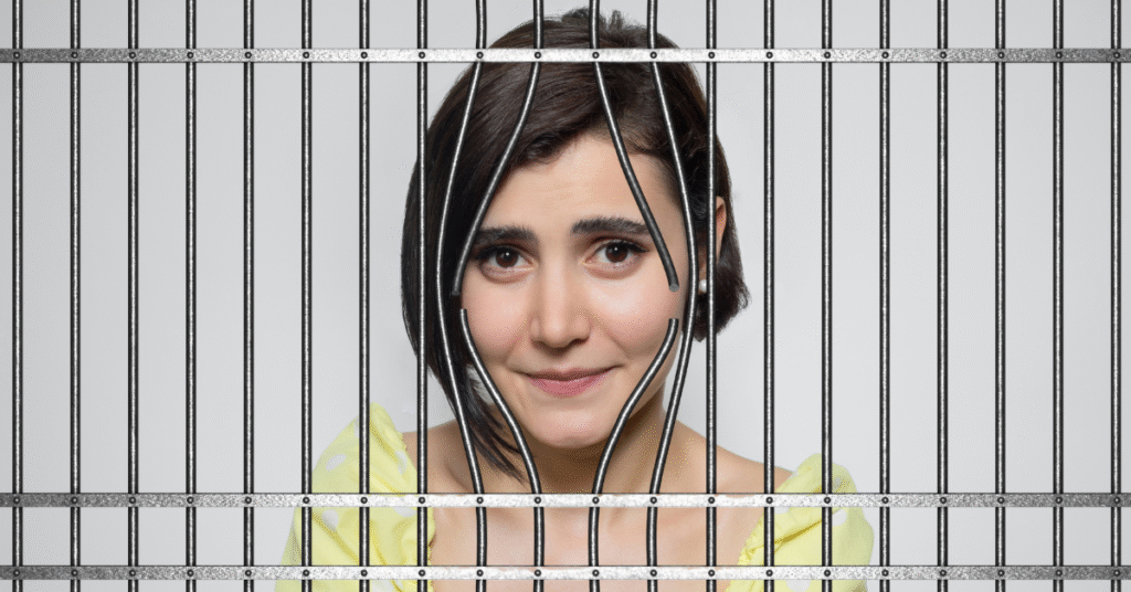 a demure-looking woman's face peeks from behind some broken prison bars