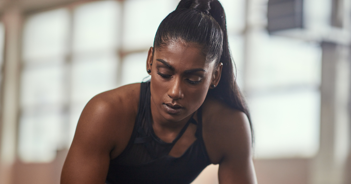 A fit-looking female athlete takes a break from a workout, looking tired.